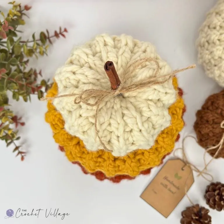 Three chunky crochet pumpkins stacked small, medium and large in rust orange, cream and mustard yellow with a cinnamon stick stem — free easy crochet pumpkin pattern in 3 sizes