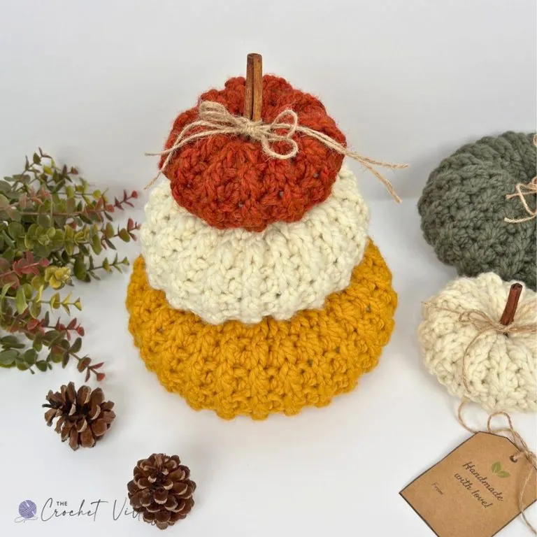 Three chunky crochet pumpkins stacked small, medium and large in rust orange, cream and mustard yellow with a cinnamon stick stem — free easy crochet pumpkin pattern in 3 sizes