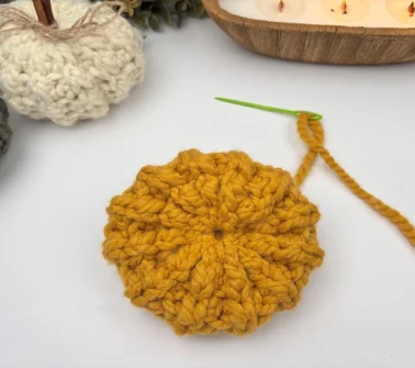 Gathering the top opening of a stuffed crochet pumpkin closed with a running stitch and yarn needle