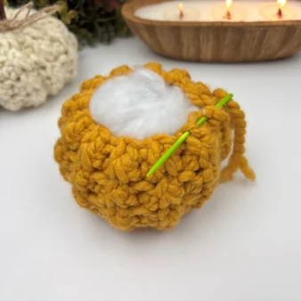 Filling a chunky crochet pumpkin with polyester fiberfill through the open top to shape it