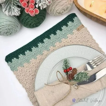 Crochet rectangle placemat in forest green, sage, and cream under a holiday place setting with napkin and cutlery