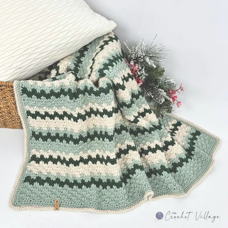 Granny spike stitch crochet blanket in forest green, sage, and cream, draped over a basket with a cream border