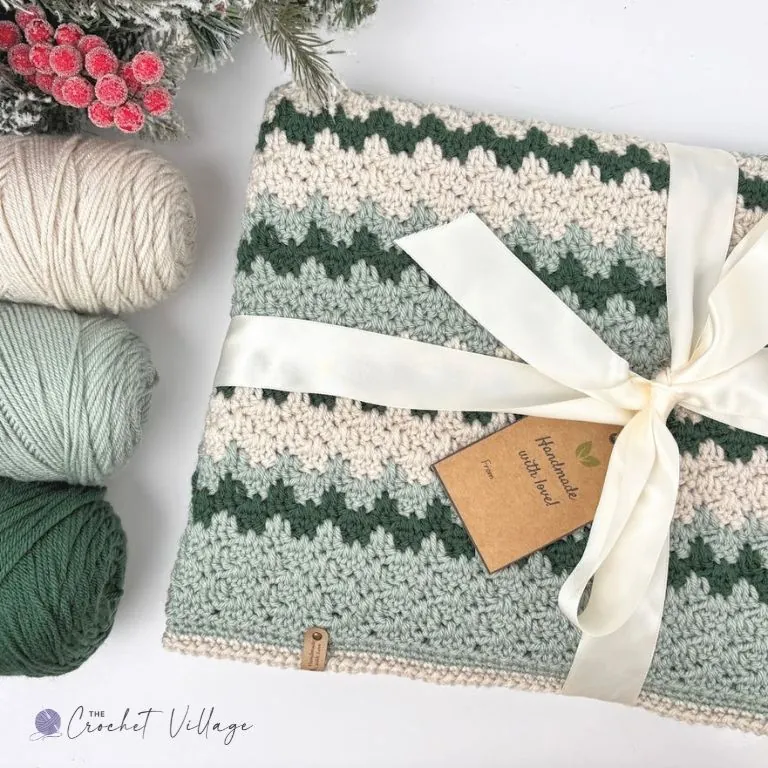 Folded crochet blanket in green and cream tied with cream ribbon and a handmade gift tag, ready to give